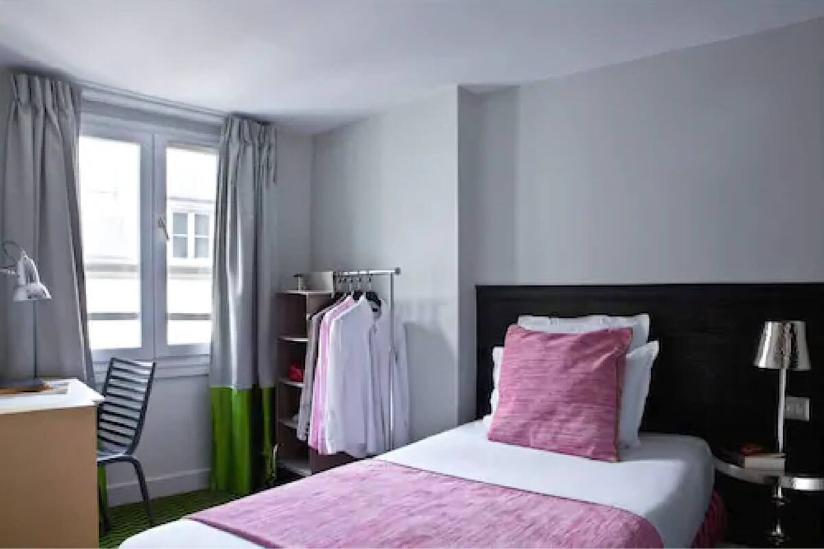 A hotel room with a bed, a desk, a chair, a wardrobe, and a window with curtains.