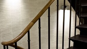 A spiral staircase with a wooden handrail and black balusters, leading to a landing with a light fixture. - Hôtel Antin Trinité (Paris)