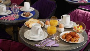 A breakfast setting with plates of croissants, eggs, and fruit, along with cups and a glass of orange juice. - Hôtel Antin Trinité (Paris)