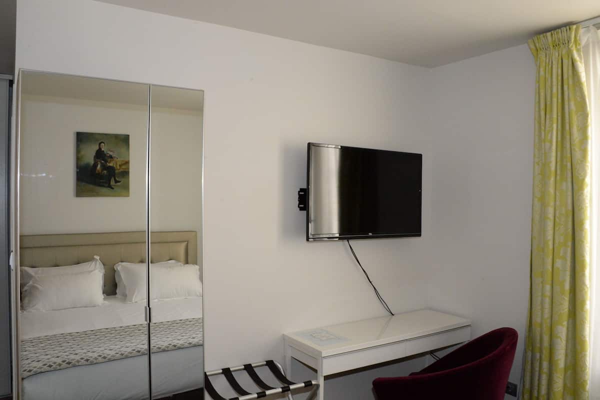 Una camera d'albergo con un letto, una scrivania, una sedia, una TV a parete e uno specchio.