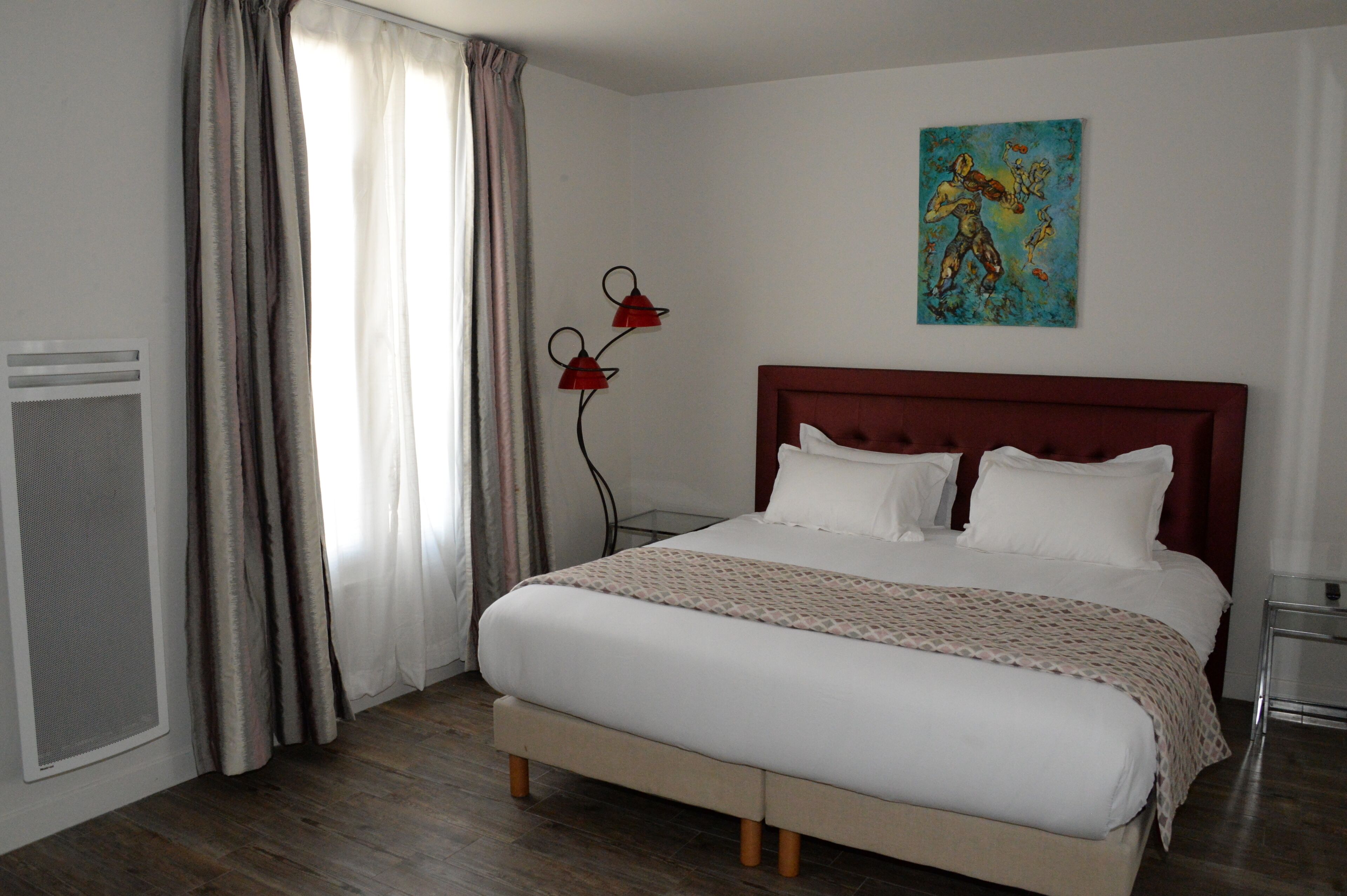 A neatly made bed with a headboard, a window with curtains, a wall-mounted artwork, and a bedside table.