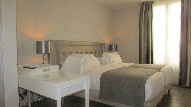 Una habitación de hotel con una cama doble, una mesita de noche, una lámpara y una ventana con cortinas.