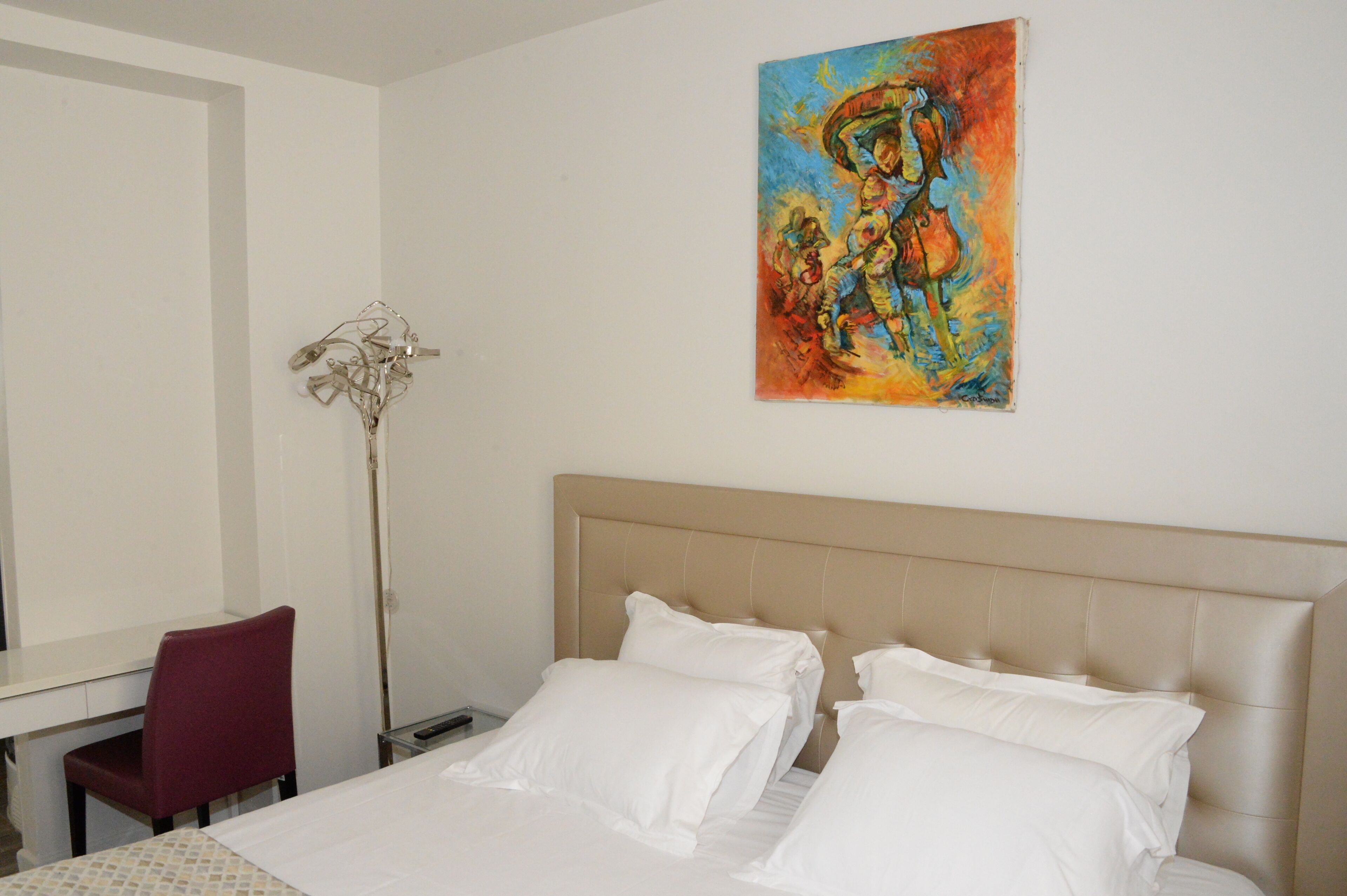 A hotel room with a bed, a desk, a chair, and a painting on the wall.