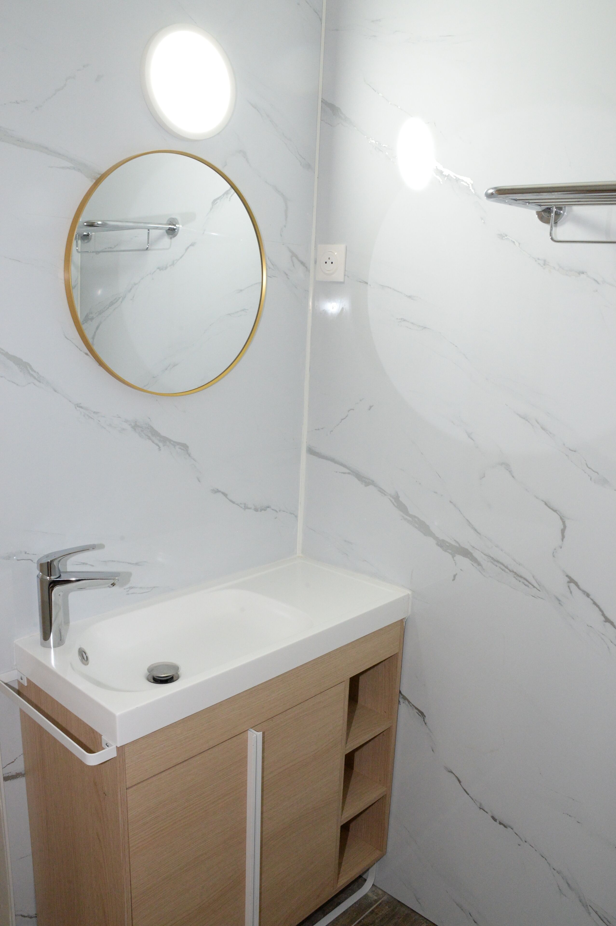 A bathroom with a white sink, a round mirror with a gold frame, and marble-patterned walls.