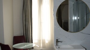 Un baño con lavamanos de mármol, un espejo redondo, ducha y una silla.