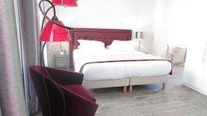 Una habitación de hotel con una cama, una silla roja, una mesita de noche y una lámpara.