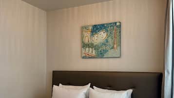 Una habitación de hotel con una cama, un cabecero, un cuadro en la pared y una lámpara del techo.