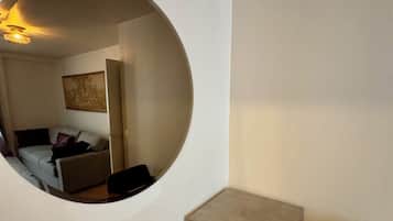 Een kamer met een rond raam, een kleine tafel, een stoel en een bank met kussens.