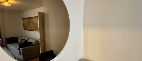 A room with a circular window, a small table, a chair, and a sofa with cushions.