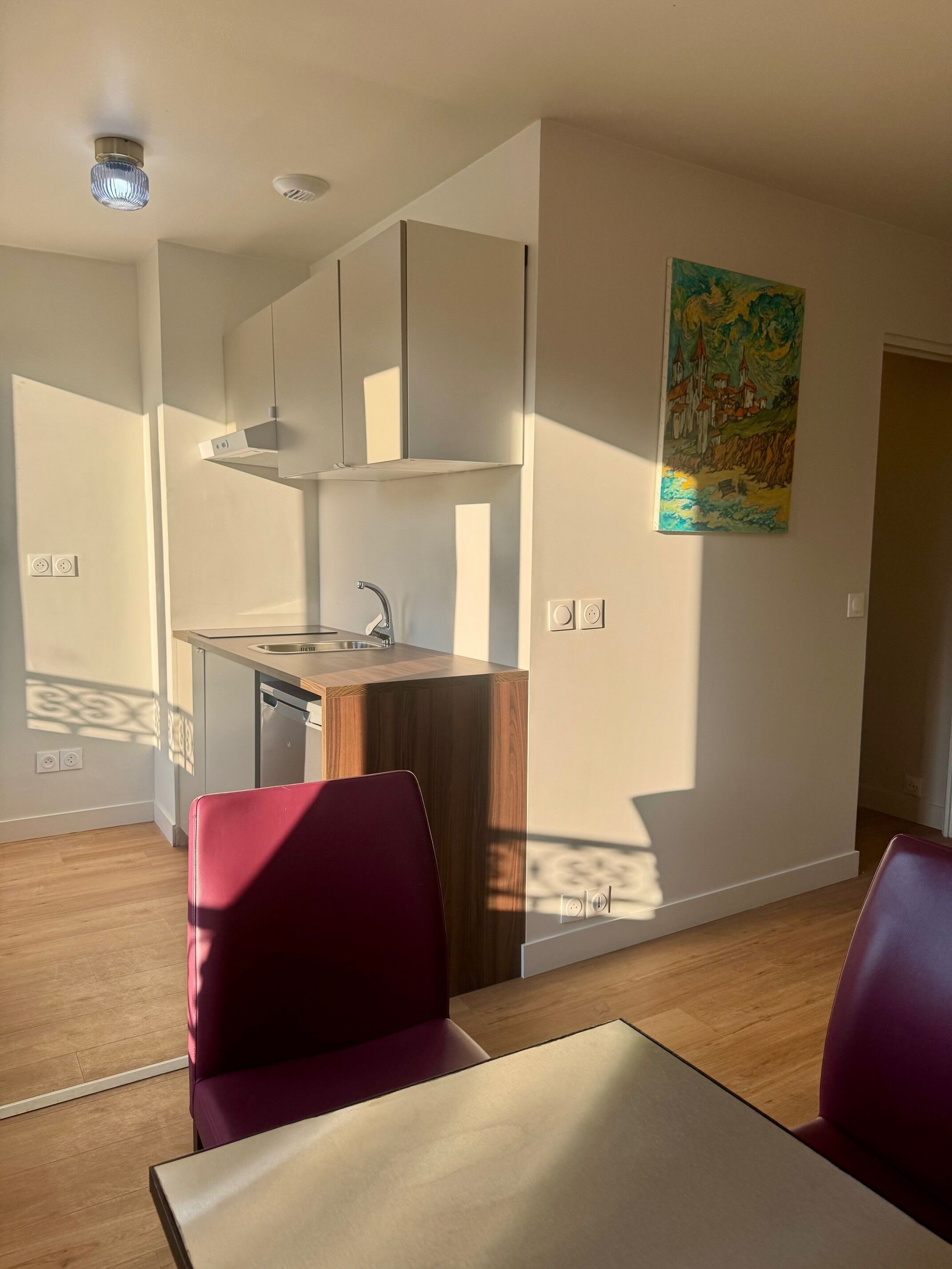 A modern kitchen with a built-in dishwasher, a dining area with a table and two chairs, and a painting on the wall.