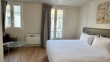 Una habitación de hotel con cama, una mesita, un sofá y una ventana con cortinas.