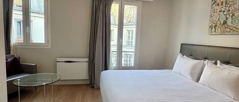 Una habitación de hotel con cama, una mesita, un sofá y una ventana con cortinas.