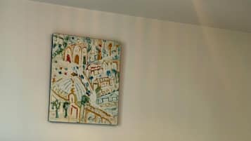 Un llit amb llenços blancs, un panell de capçal fosc i un quadre penjat a la paret que representa un paisatge urbà.