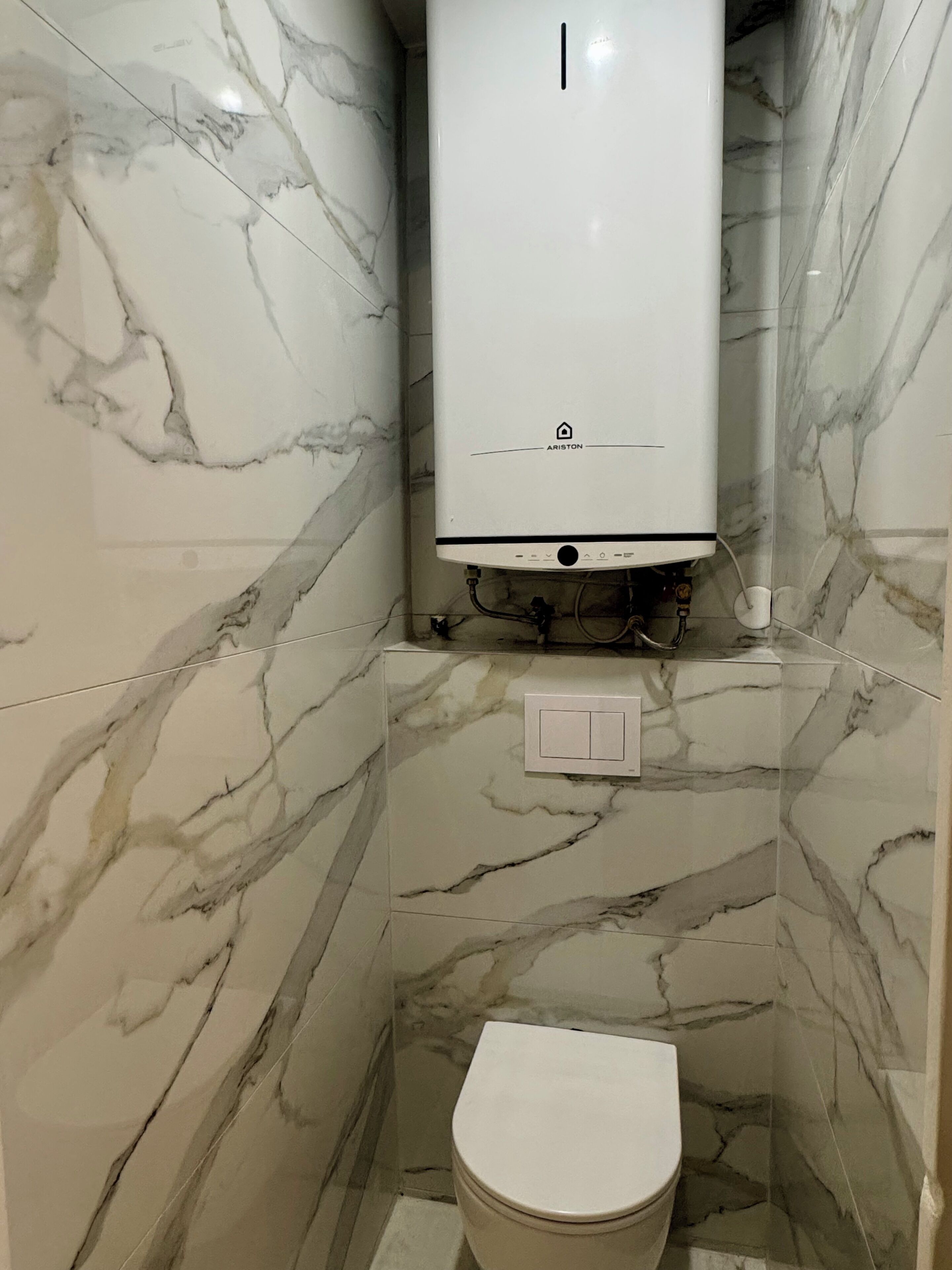 A bathroom with a white toilet, marble walls, and a white water heater.