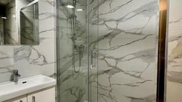 A bathroom with a glass-enclosed shower, marble walls, a white sink, and a mirror.