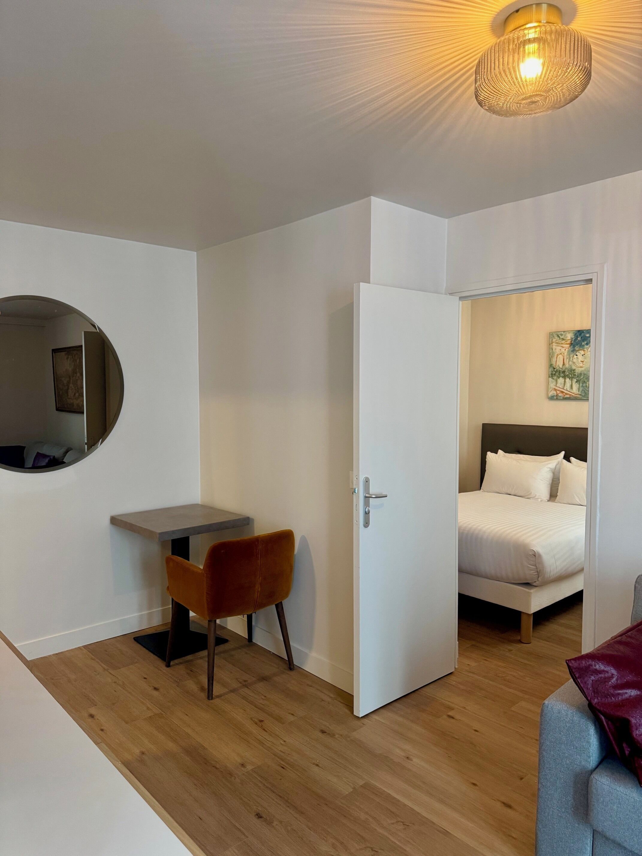 A room with a bed, a desk, a chair, and a round mirror.