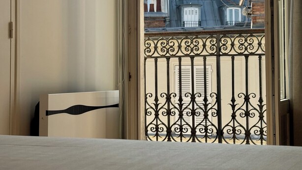 Une pièce avec vue sur un bâtiment à coupole, visible à travers une fenêtre ornée d’un balcon en fer forgé.