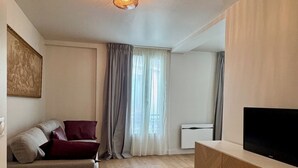 Un salon avec un canapé, un téléviseur posé sur un meuble en bois et un luminaire au plafond.
