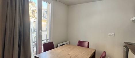 A dining area with a wooden table and four chairs, a window with curtains, and a ceiling light fixture.