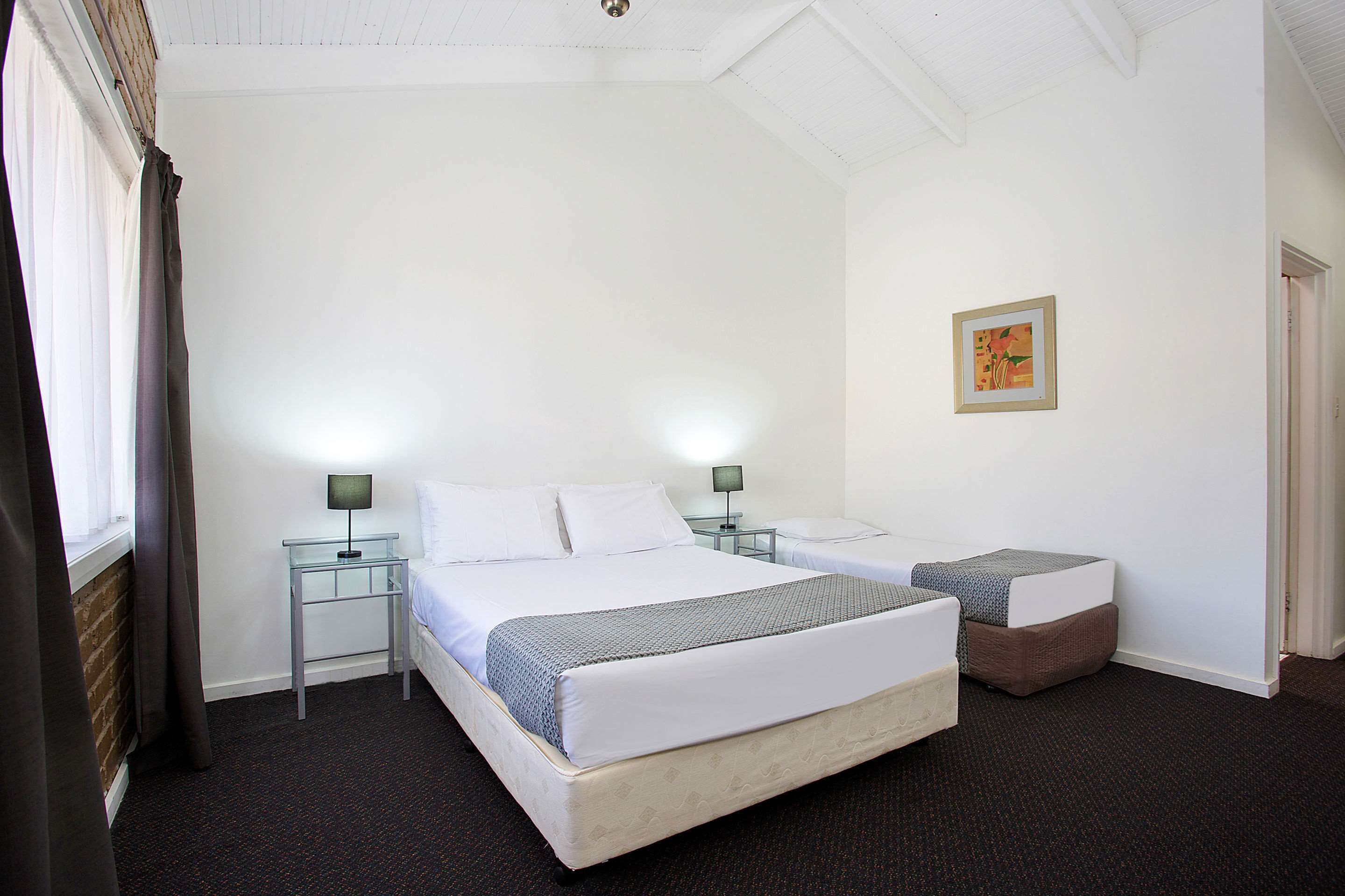 A hotel room with two beds, a small table, and a nightstand with lamps.