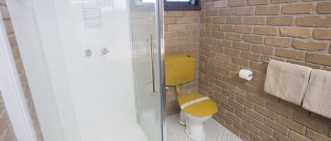 A bathroom with a glass shower enclosure, a yellow toilet, a brick wall, and a towel rack.