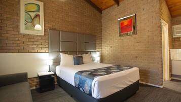 A bedroom with a brick wall, a bed with a headboard, a nightstand, and a lamp.