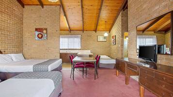 A hotel room with two beds, a dining table with chairs, a TV, and a wooden dresser.