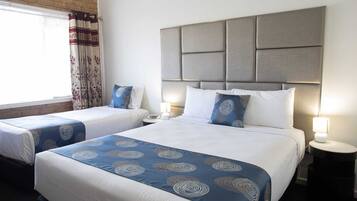 Habitación de hotel con dos camas, cada una con cubrecama azul estampado y almohadas blancas. La habitación tiene un cabecero moderno y lámparas de noche.