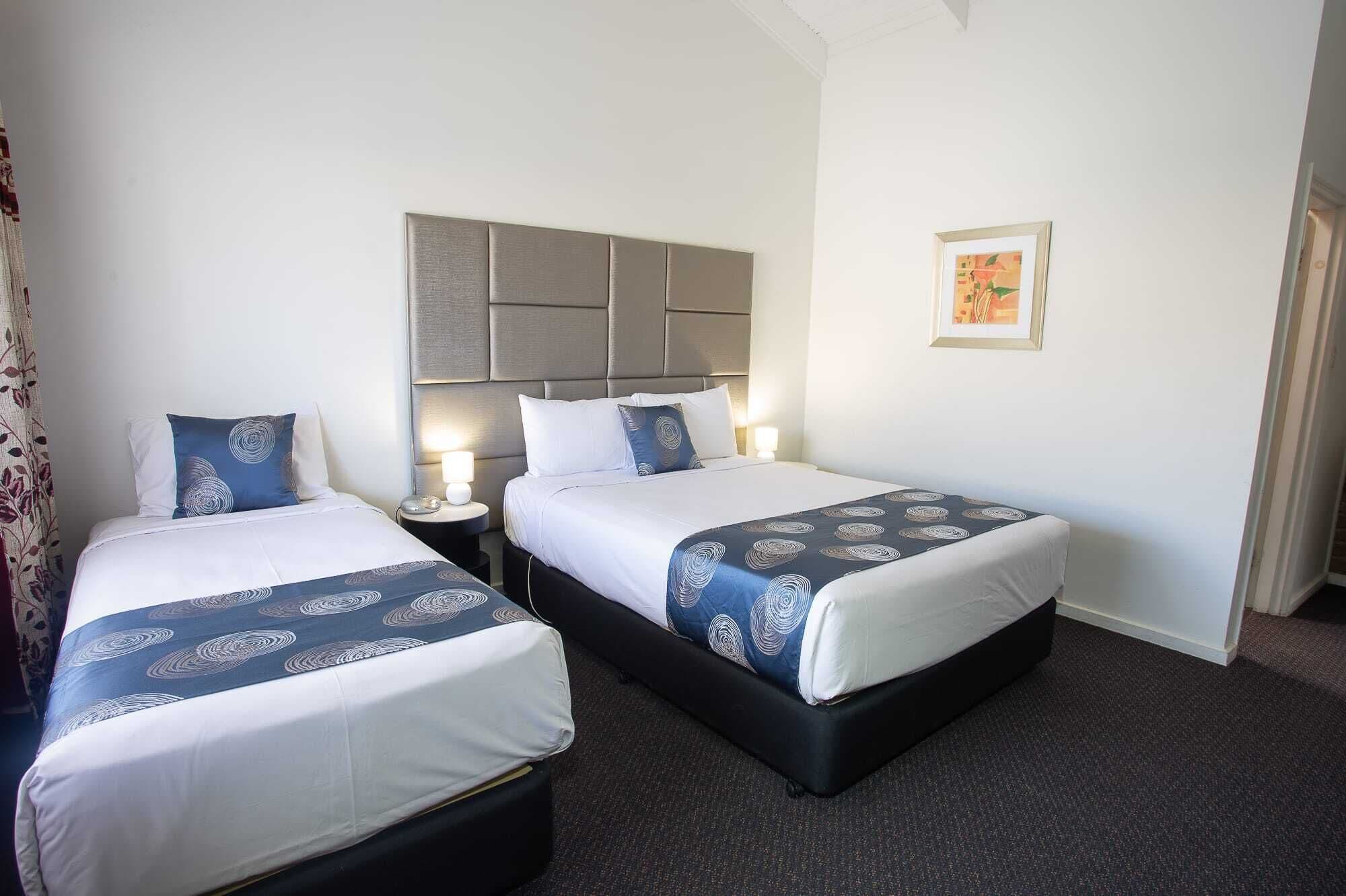 A hotel room with two beds, each with a headboard, bedside tables with lamps, and a framed picture on the wall.