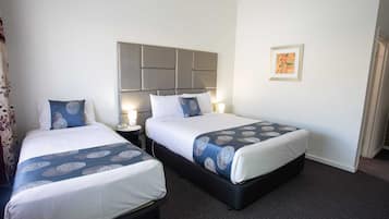 A hotel room with two beds, each with a headboard, bedside tables with lamps, and a framed picture on the wall.