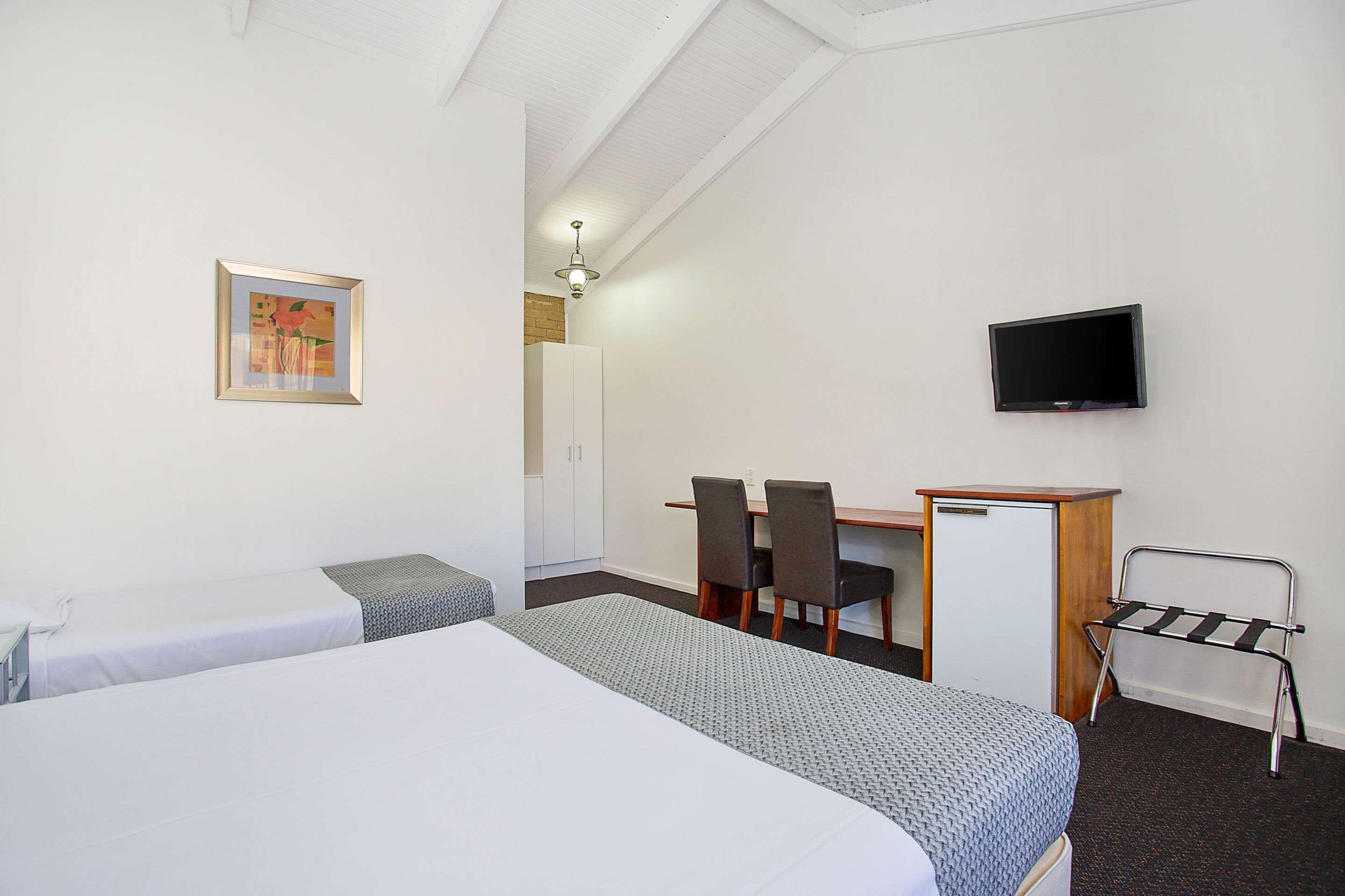 A hotel room with two beds, a desk, a chair, a TV, and a coat rack.