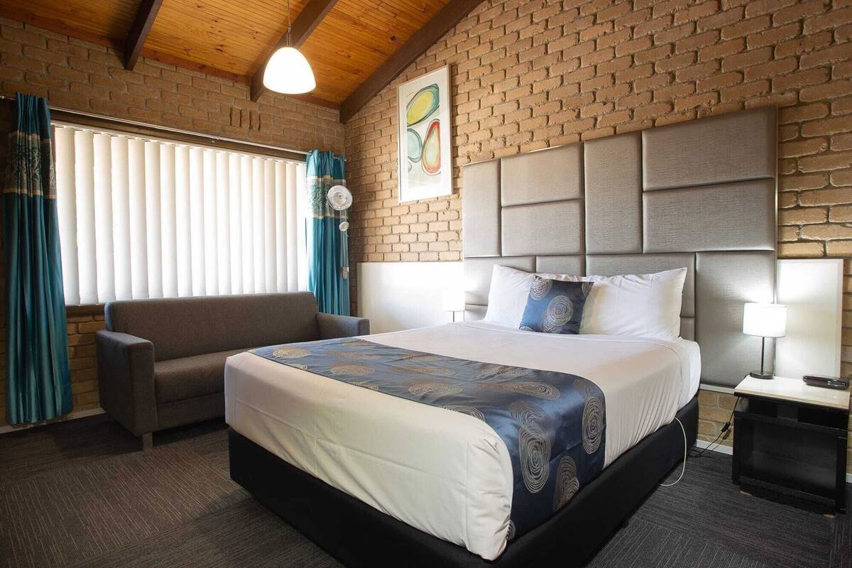 A hotel room with a bed, a sofa, a brick wall, and a window with curtains.