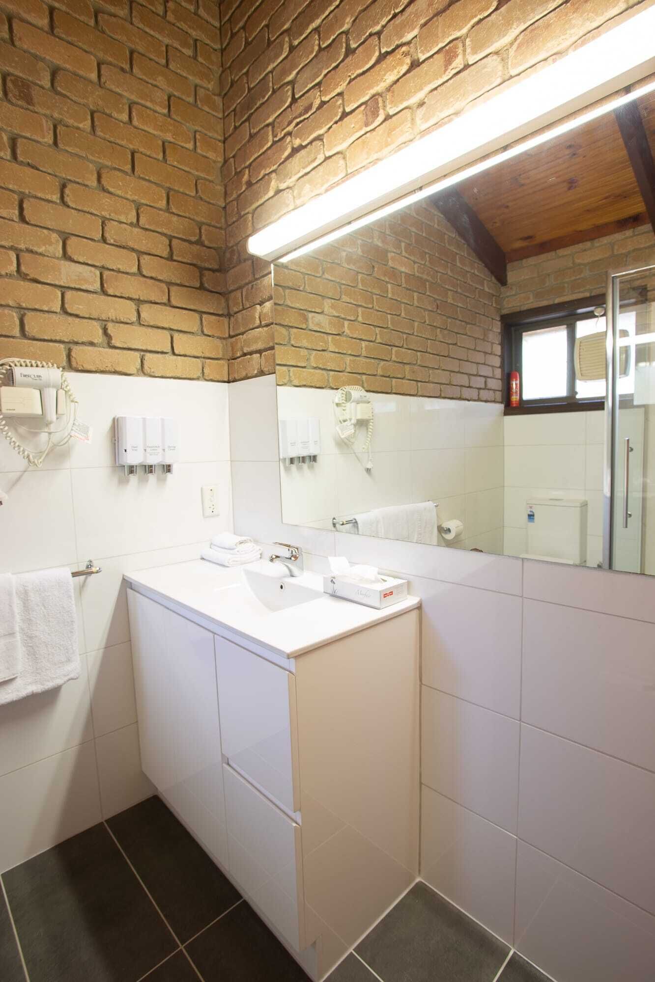 A bathroom with a white sink, a mirror, and a brick wall. There is a towel rack and a fire extinguisher visible.