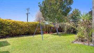 Enjoy a serene outdoor space with a swing set, lush green grass, and a variety of plants and trees.