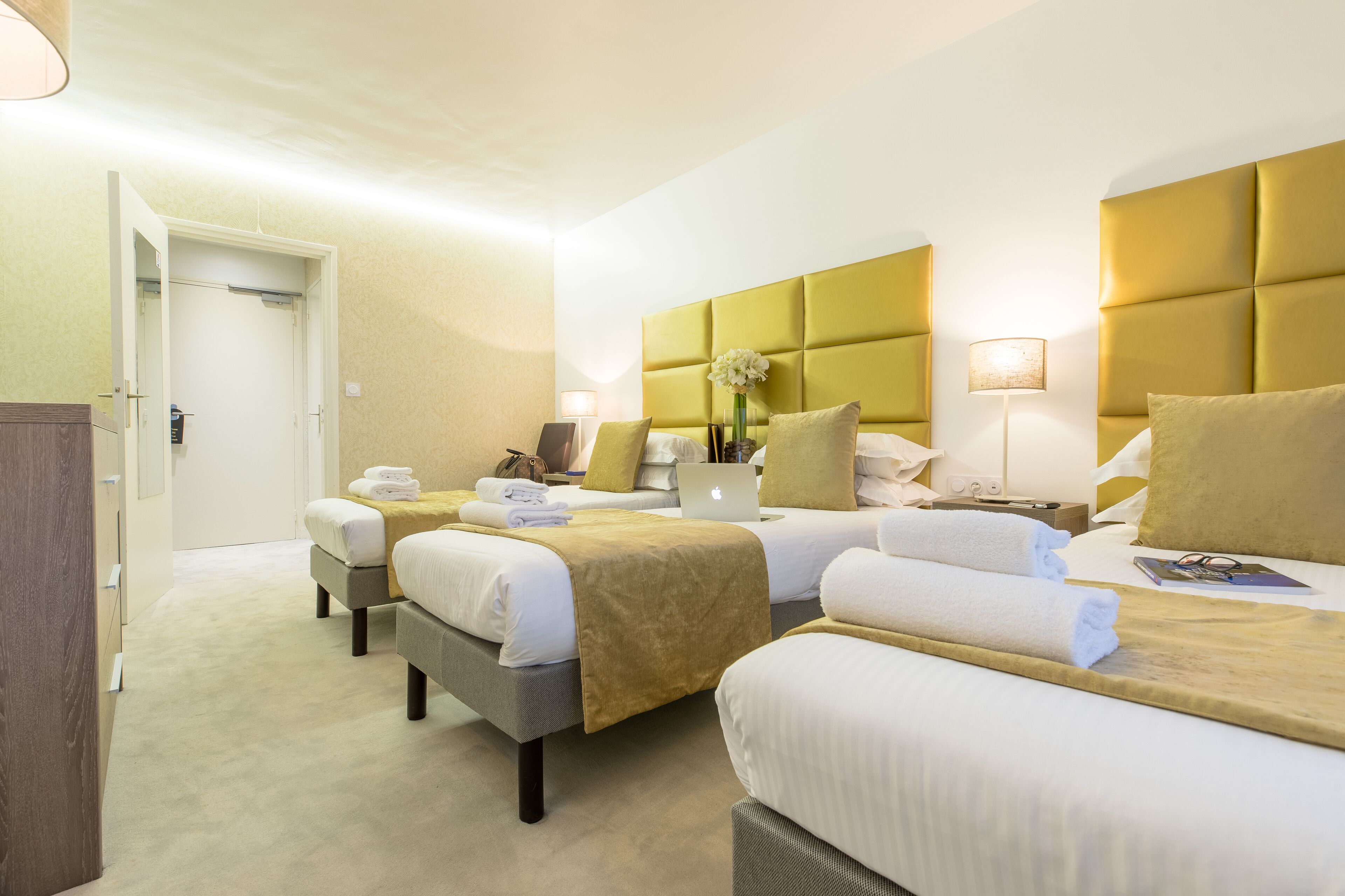 Una camera d'albergo con tre letti, ognuno con una diversa decorazione della testiera, e una porta che dà su un corridoio.