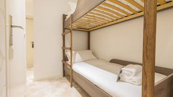 Una cama litera con estructura de madera, ropa de cama blanca y una toalla en la cama inferior.