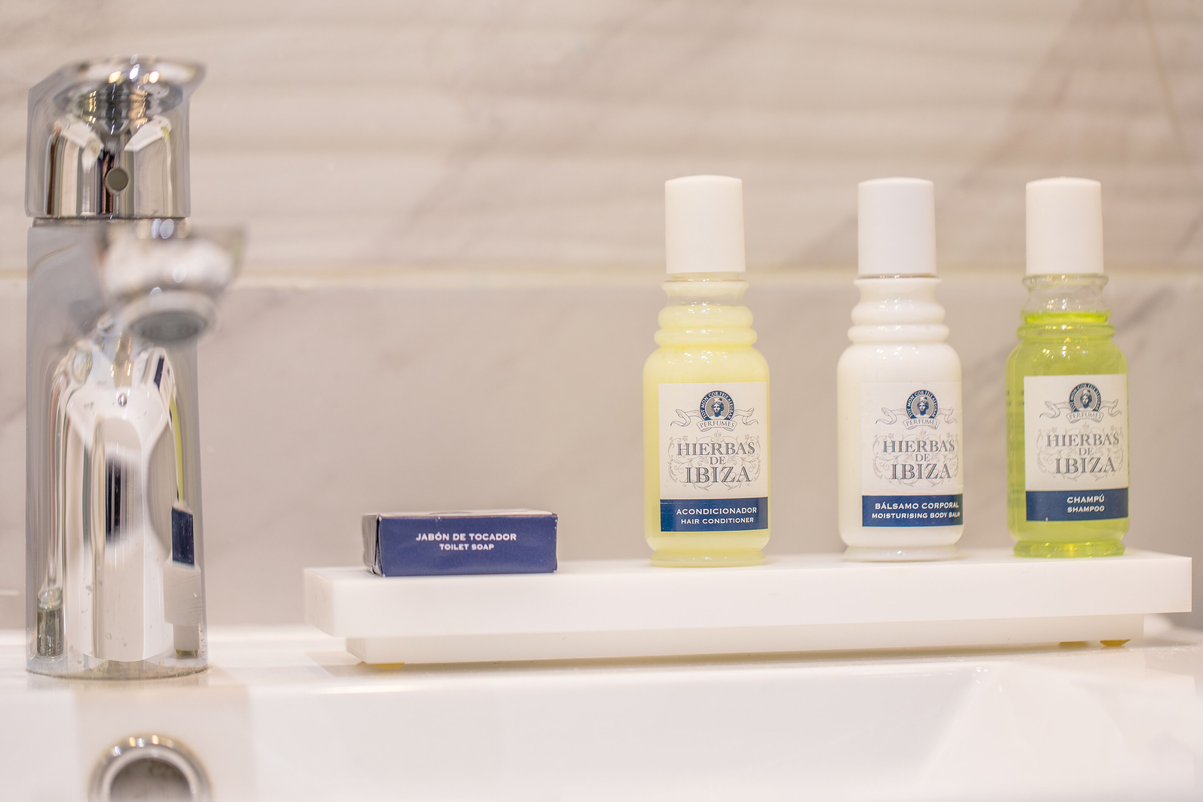 Un estante de baño con tres botellas de acondicionador capilar Hierbas de Ibiza, una botella de loción corporal Hierbas de Ibiza y una pastilla de jabón de baño Hierbas de Ibiza.