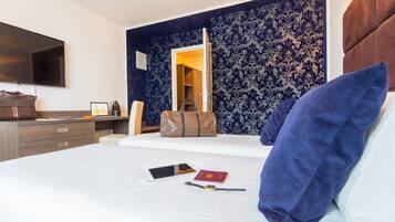 Une chambre d’hôtel comprenant un lit, une table de chevet, une télévision, une armoire et une salle de bain visible à travers une porte ouverte.