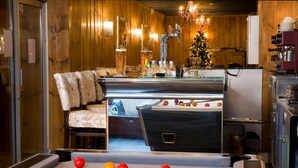 Una mesa de billar con bolas, un sofá, un árbol de Navidad y una zona de cocina con un refrigerador.