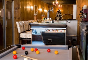 A pool table with balls, a sofa, a Christmas tree, and a kitchen area with a refrigerator.