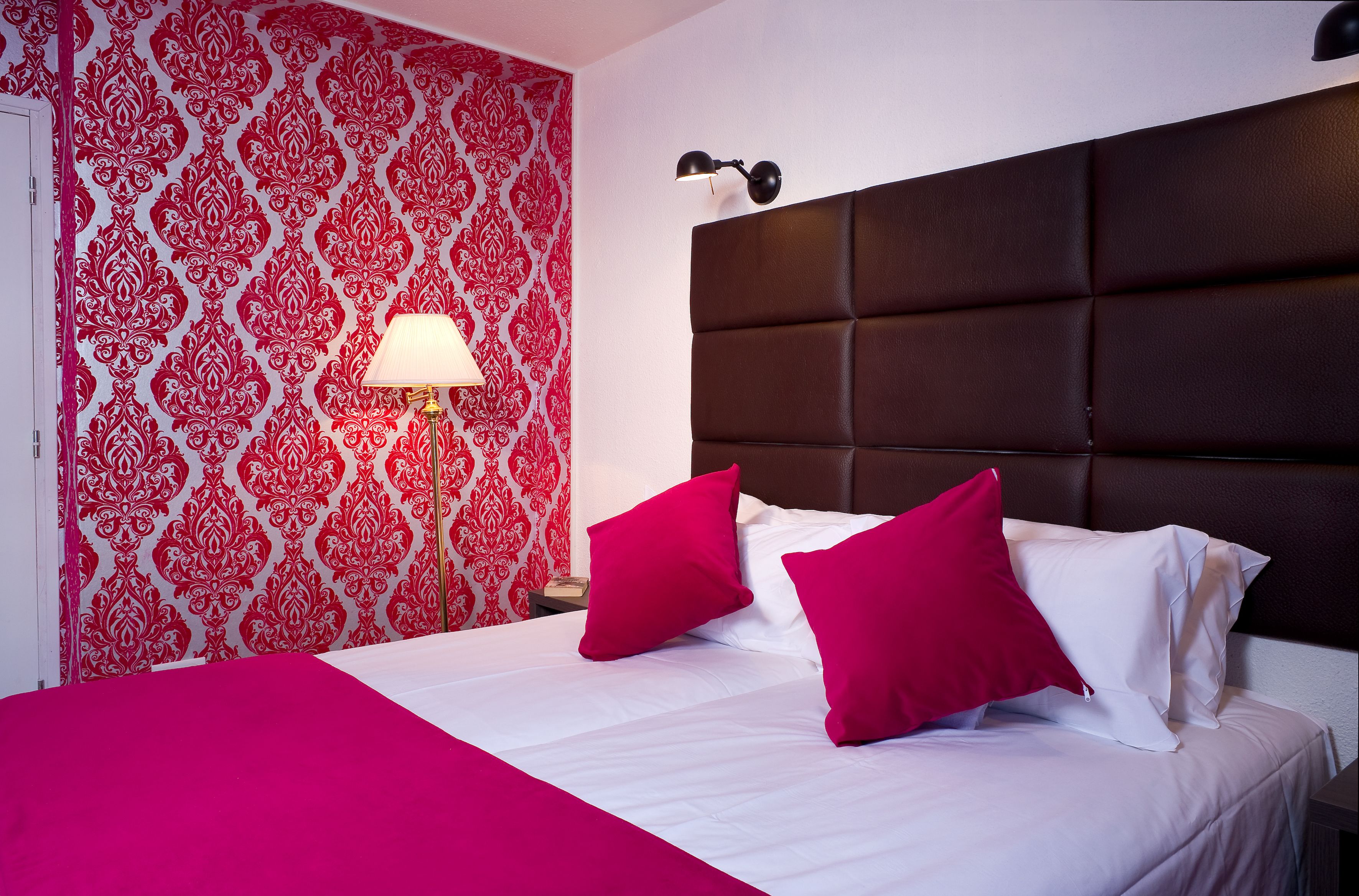 Una cama bien hecha con una colcha blanca y roja, dos almohadas rojas y un cabecero marrón.