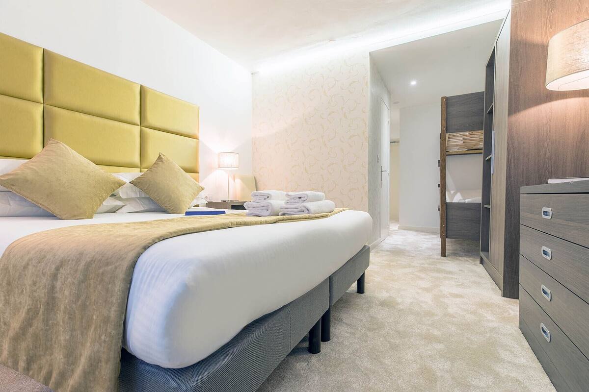 Una habitación de hotel con una cama grande, una mesita de noche con lámpara, un armario y un vestidor.