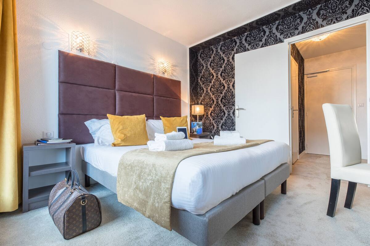 Una habitación de hotel con una cama grande, una mesita de noche, una lámpara, una silla y una maleta.