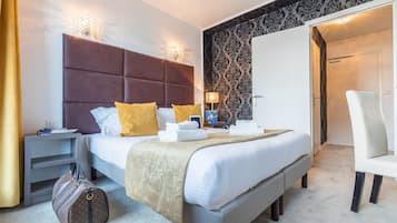 Ein Hotelzimmer mit einem großen Bett, einem Nachttisch, einer Lampe, einem Sessel und einem Koffer.