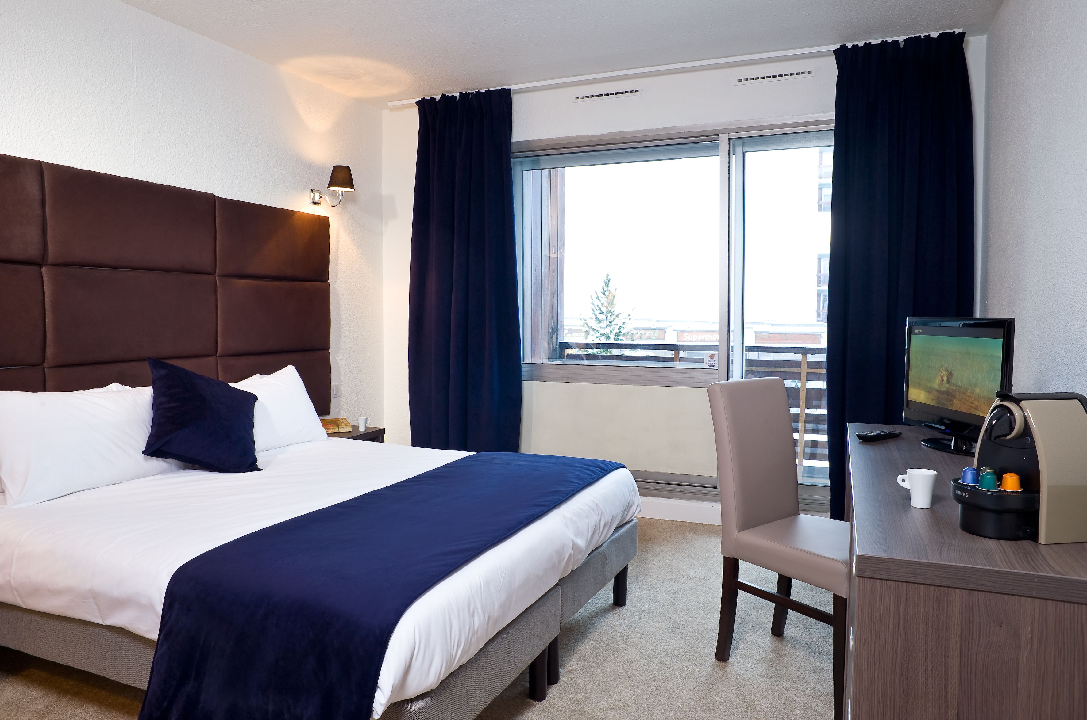 Ein Hotelzimmer mit einem Bett, einem Schreibtisch, einem Sessel, einem Fernseher und einer Kaffeemaschine.