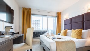 Habitación de hotel con cama, escritorio, silla, televisión de pantalla plana y ventana con cortinas.