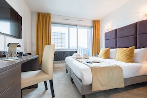 A hotel room with a bed, a desk, a chair, a flat-screen TV, and a window with curtains.