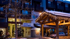 Un hôtel avec une enseigne indiquant « Hôtel Olympic », un espace extérieur couvert illuminé et de la neige au sol.