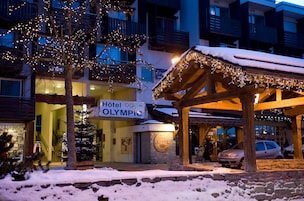 A hotel with a sign reading "Hotel Olympic," a covered outdoor area with lights, and snow on the ground.