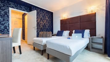 Ein Hotelzimmer mit zwei Betten, einem Schreibtisch und einem Stuhl. Auf einem Bett liegt ein Laptop.